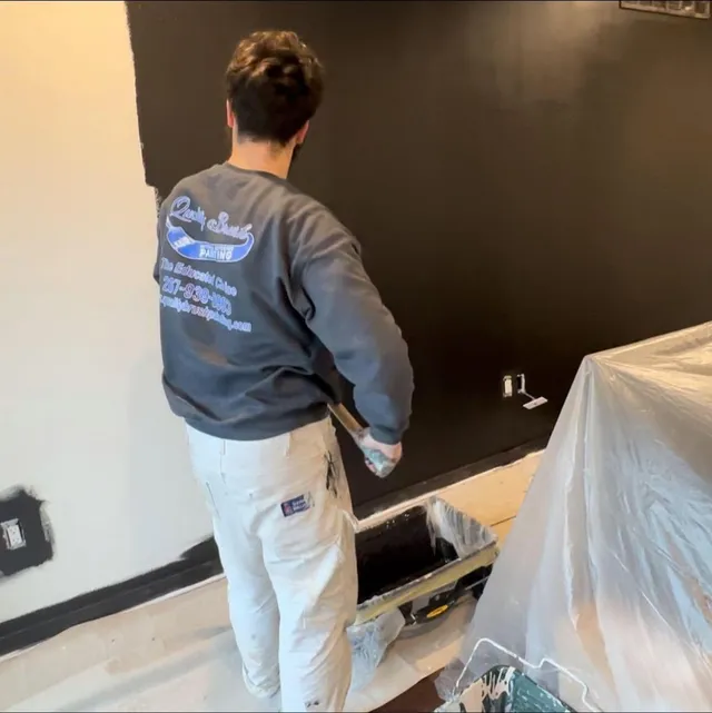 Quality Brush Painting crew member rolling a dark accent wall with floors fully covered
